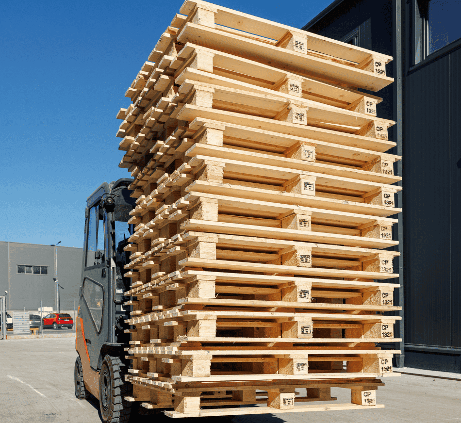 Large stack of wooden pallets loaded on forklift at warehouse.